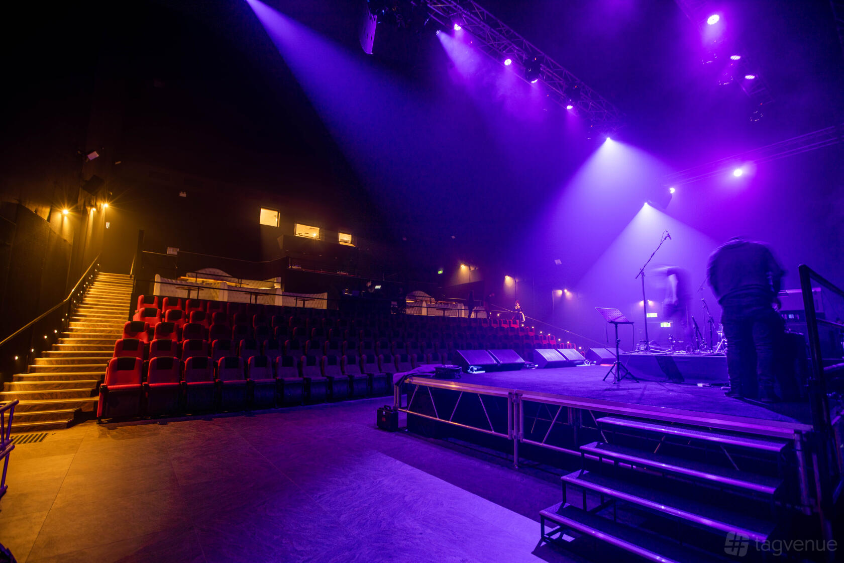 A bar with theater seating, a stage with microphones, and purple stage lighting at Planet Royale.