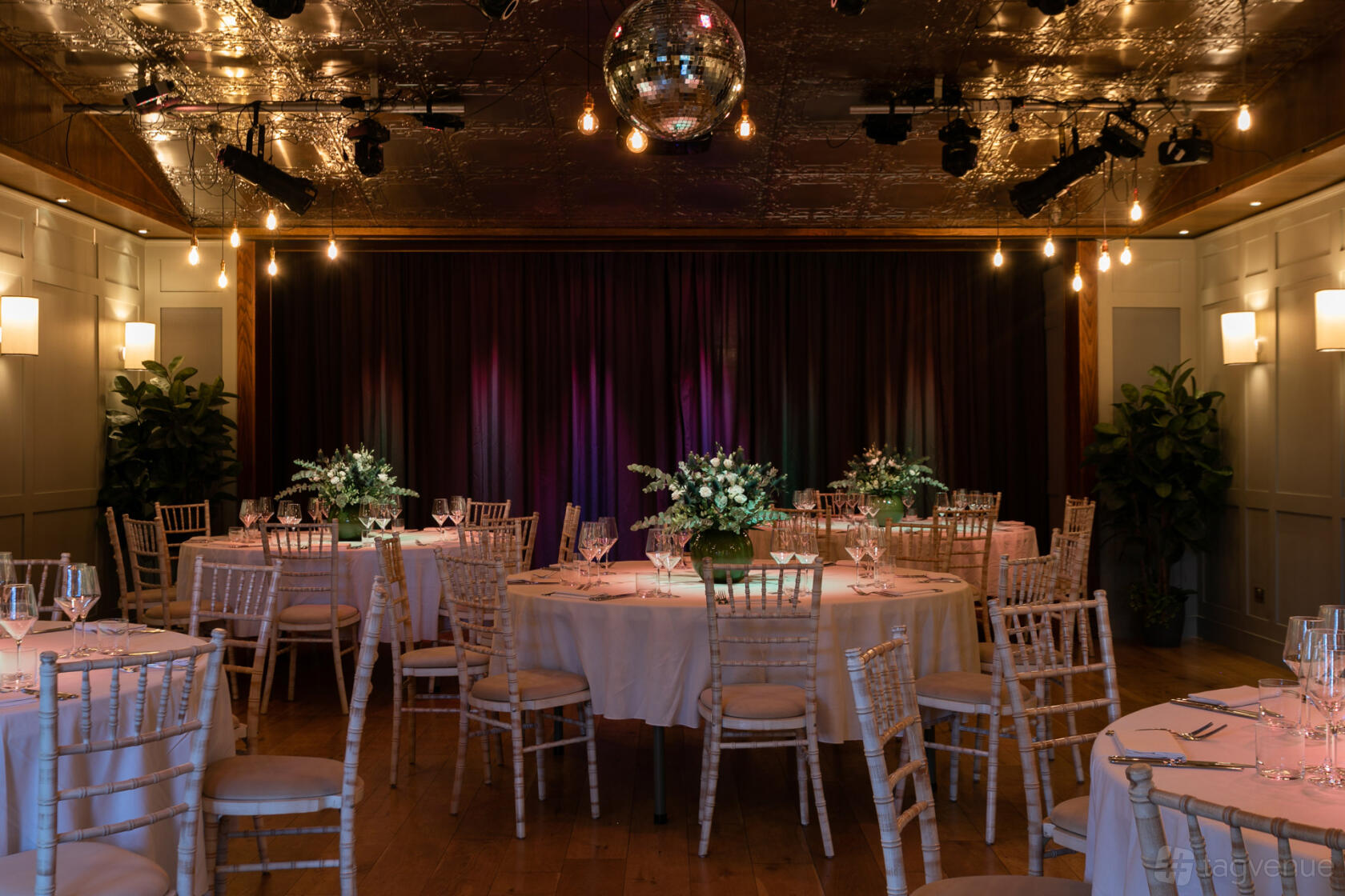 An event space in a bar with round tables, floral centerpieces, a disco ball, and stage lighting at Century Club.