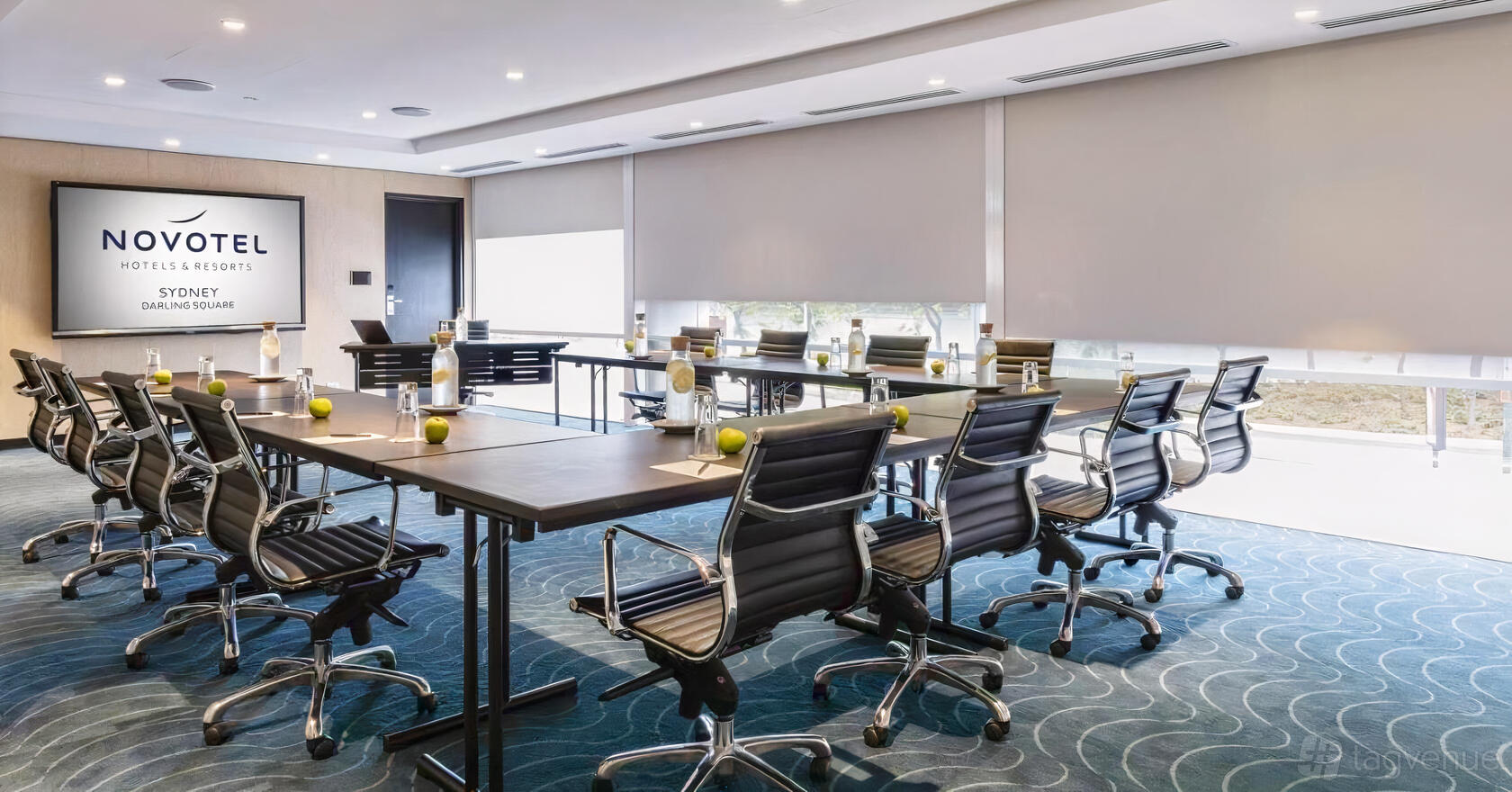 A hotel meeting room with conference tables, ergonomic chairs, and bottled water at Novotel Sydney Darling Square.