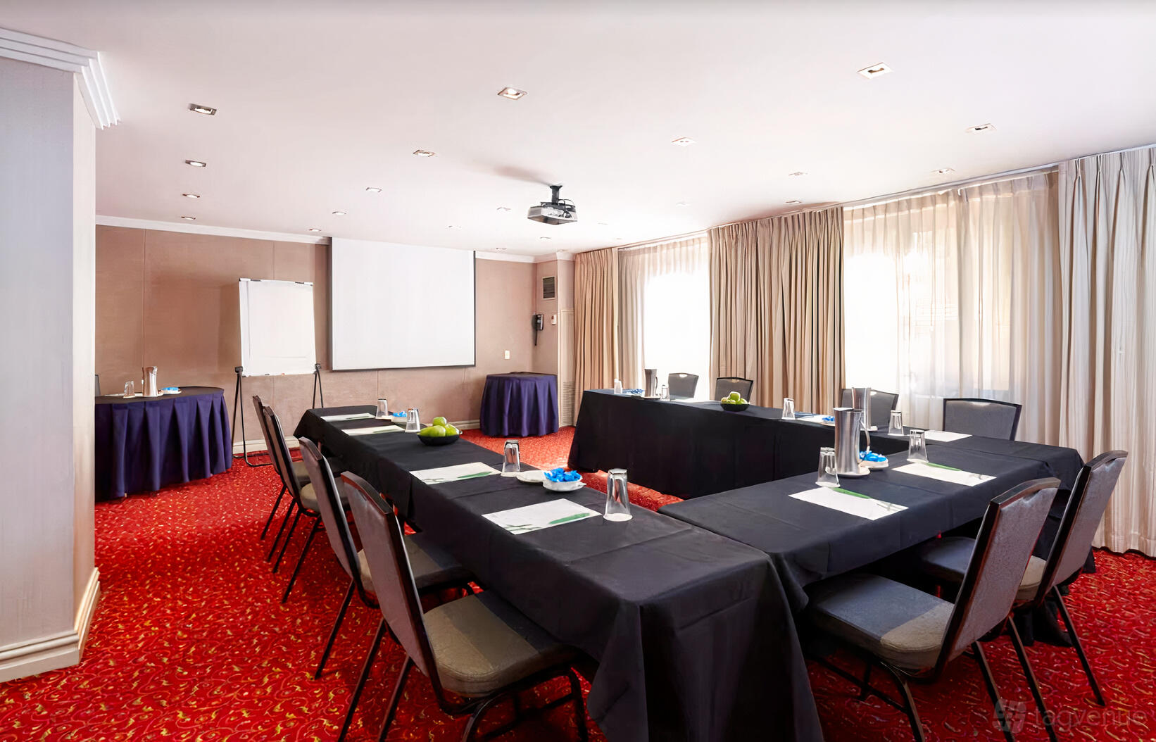 A hotel meeting room with U-shaped tables, black tablecloths, red carpet, and natural light at Holiday Inn Parramatta.