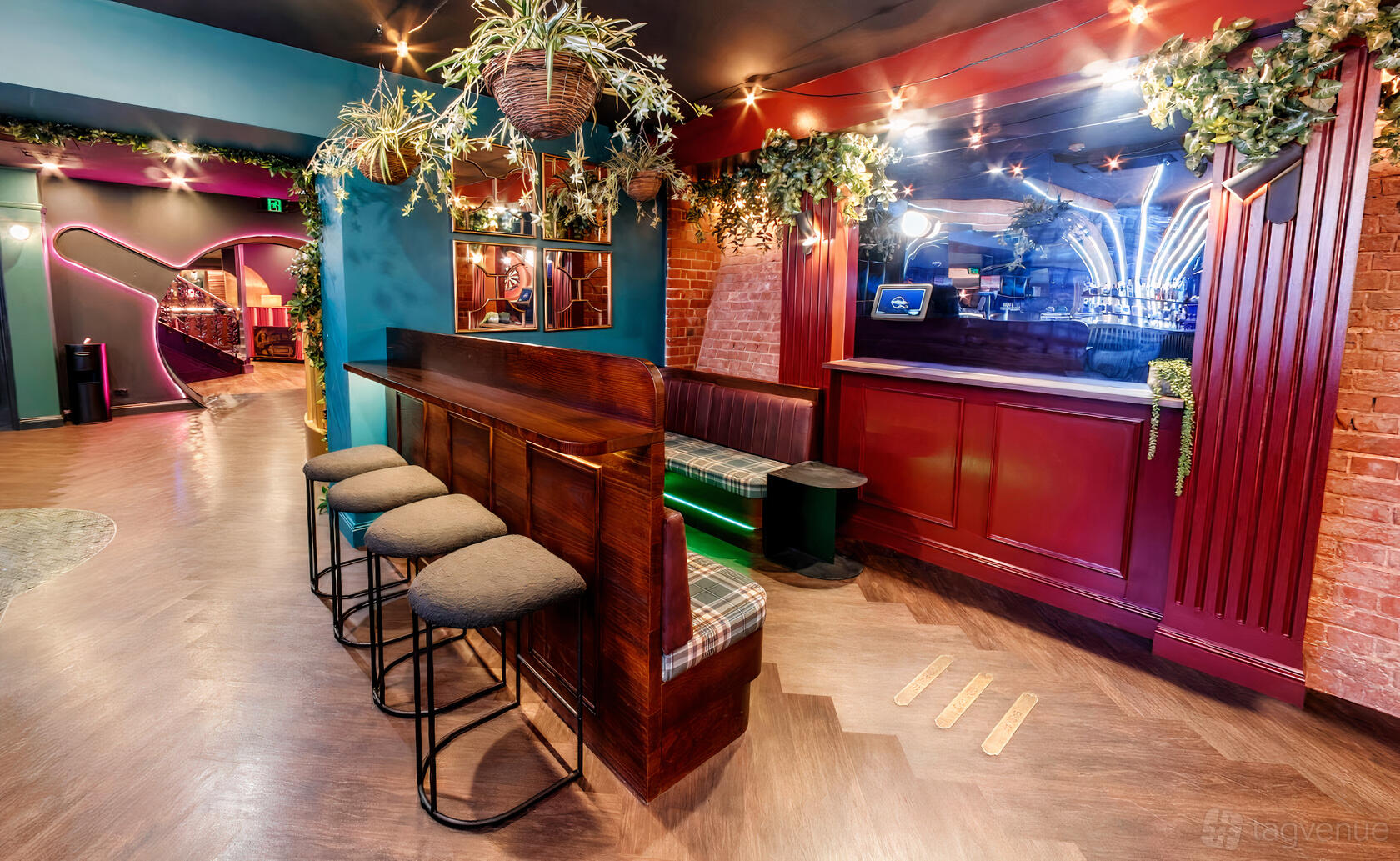 An event space in a bar with a wooden bench, bar stools, hanging greenery, and mirrored red paneling at Ballers Clubhouse Adelaide.