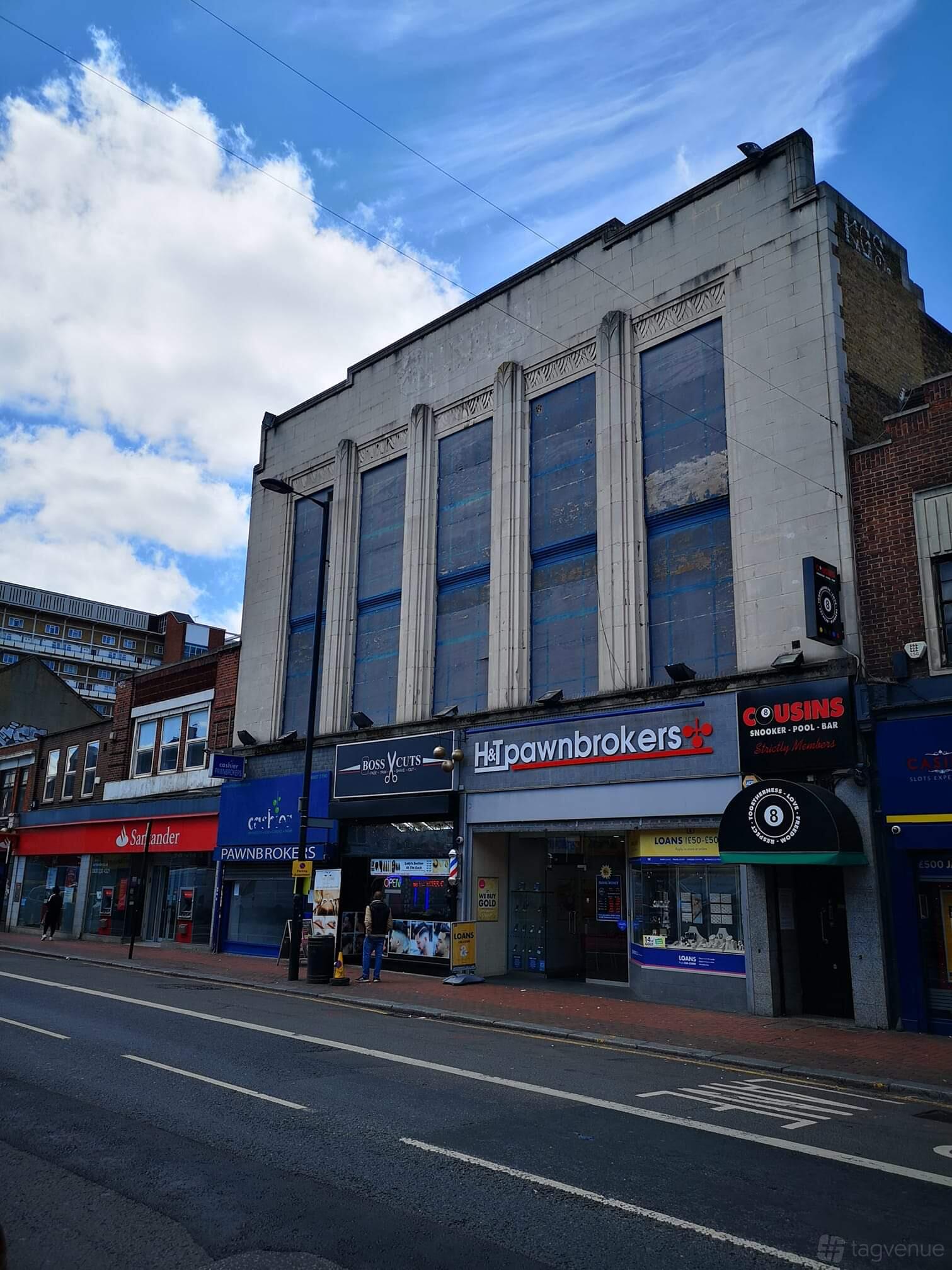 A pub and bar housed in an art deco building with tall windows and retail shops on the ground floor at Cousins snooker and pool club.