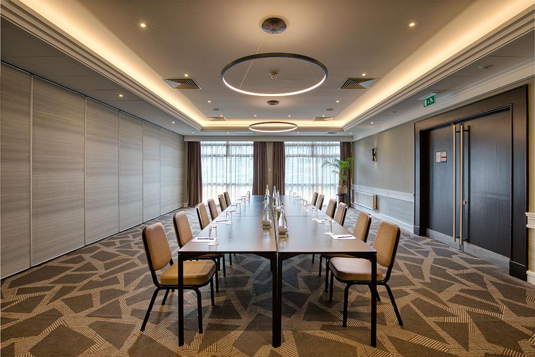 An event space with geometric patterned carpet, U-shaped conference table, and circular ceiling lights at DoubleTree by Hilton London - Ealing.