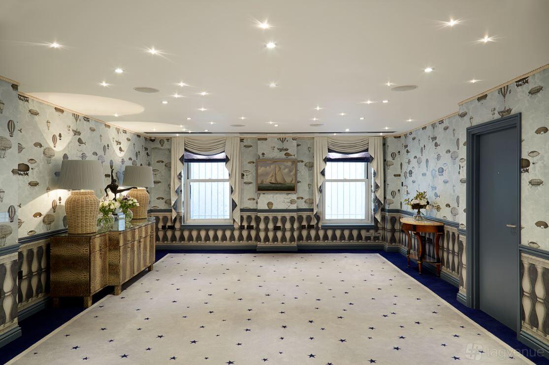 An event space with nautical-themed wallpaper, blue carpeting, and two large windows at The Mandeville Hotel.