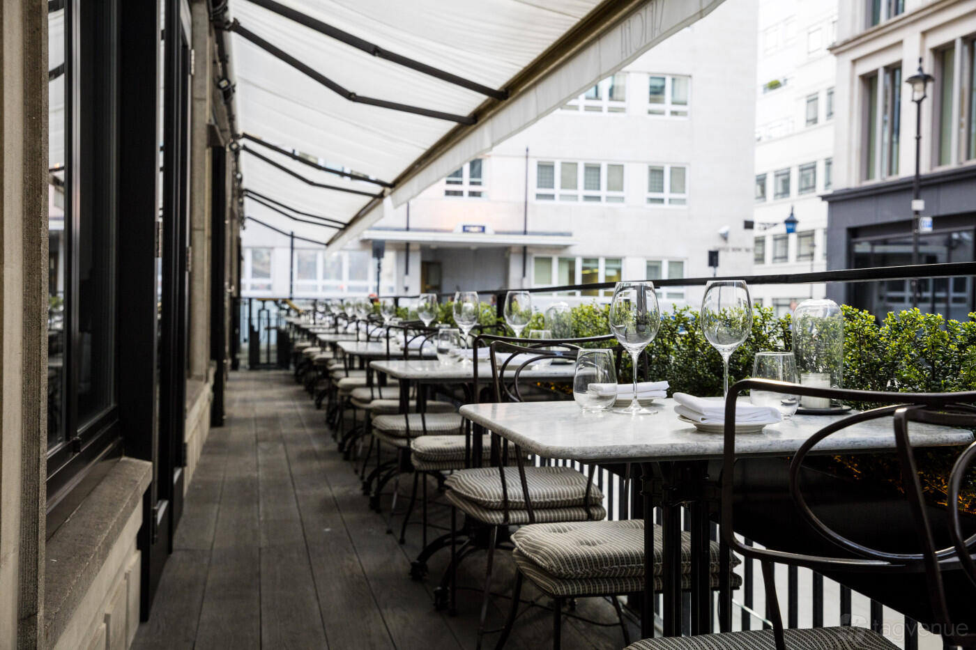 A restaurant patio with marble-topped tables, woven chairs, and a striped awning at Sartoria.