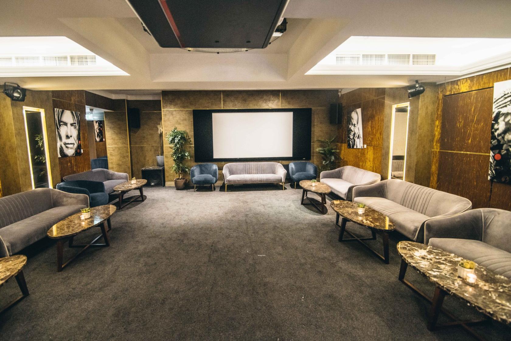 A cinema room with plush velvet sofas, marble coffee tables, and a projection screen at Karma Sanctum Soho Hotel.