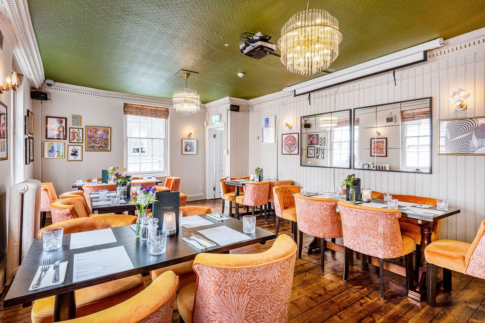 A function room with coral velvet chairs, wooden floors, chandeliers, and art-lined walls at The Market Tavern.
