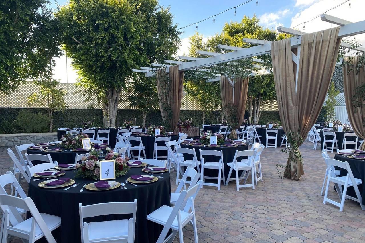 An outdoor event venue with round tables, white chairs, draped pergola, and string lights at Fletcher Courtyards.