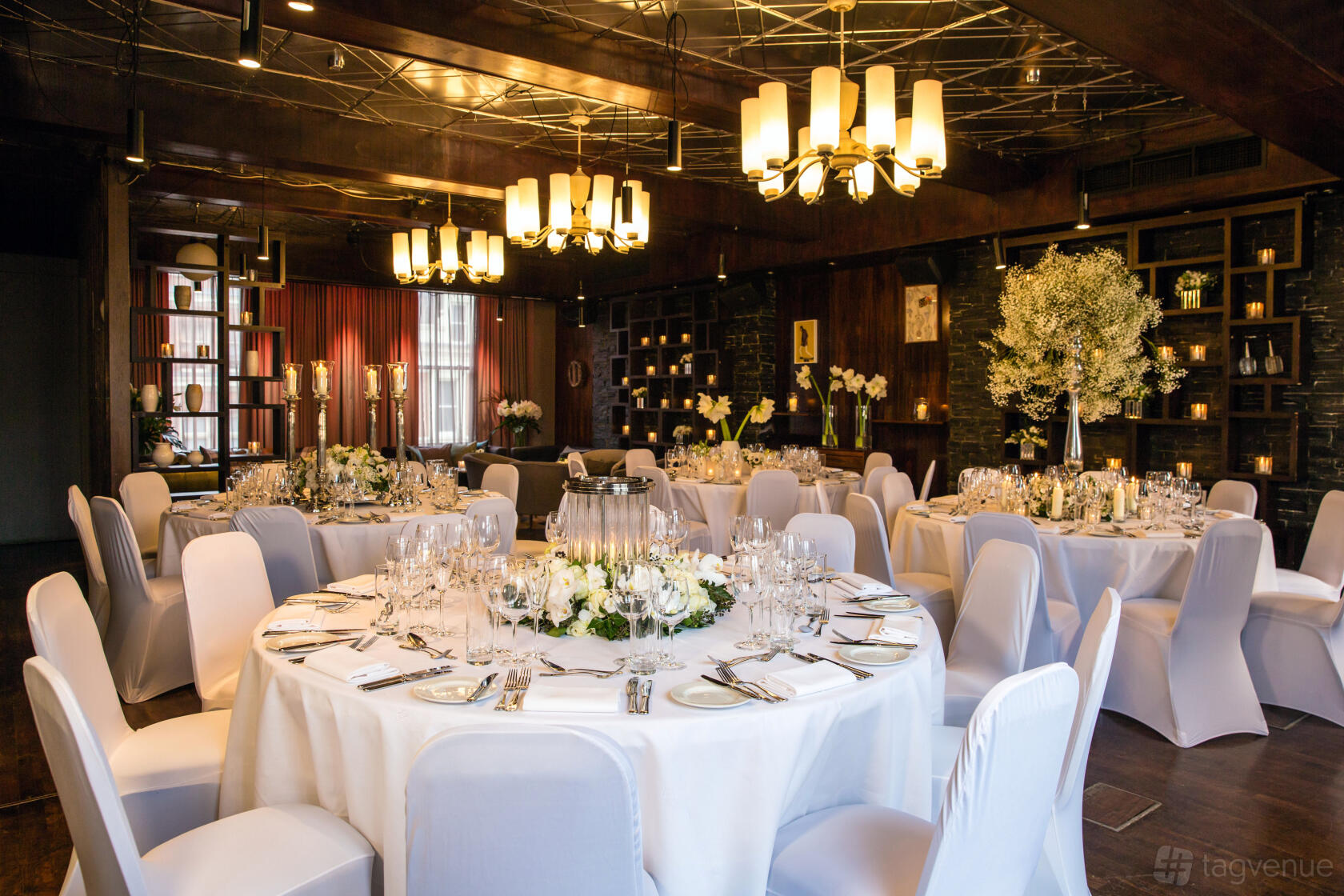An event space in a bar with round tables dressed in white linens, floral centerpieces, and modern chandeliers at Century Club.