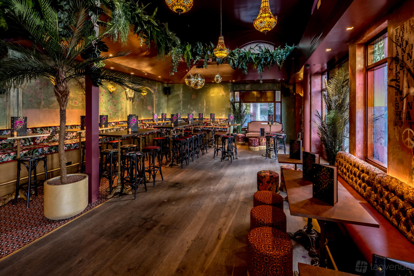A cocktail bar with lush greenery, hanging lamps, patterned seating, and wooden floors at The Cocktail Club Canary Wharf.
