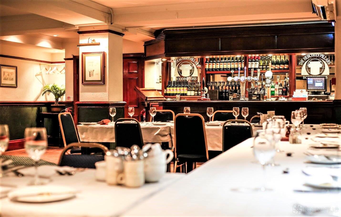 A function room in a pub with banquet tables draped in white linens, set with glassware and a full bar at The Hercules Pillars.