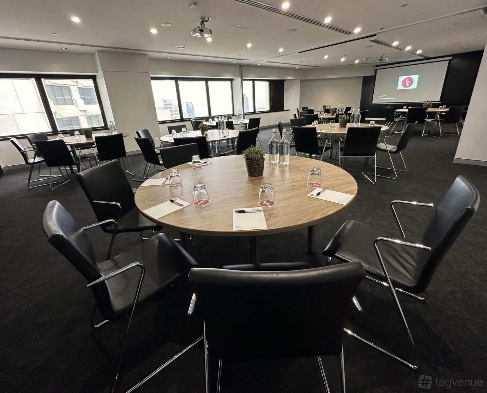 A conference centre with round tables, black chairs, and large windows providing city views at Karstens Brisbane.