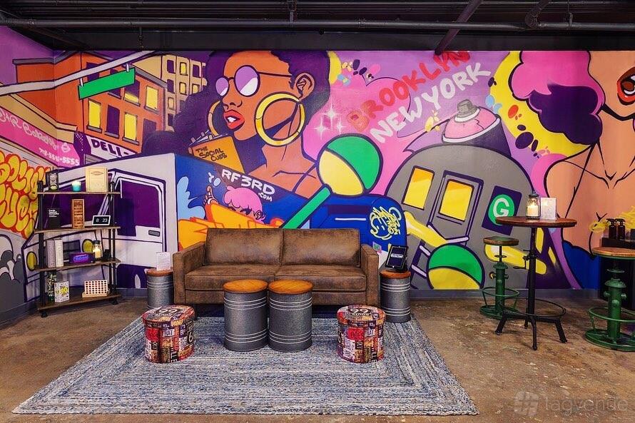 An event venue lounge with a brown leather sofa, graffiti mural walls, and metal drum tables at Social Cues - B.S.A.
