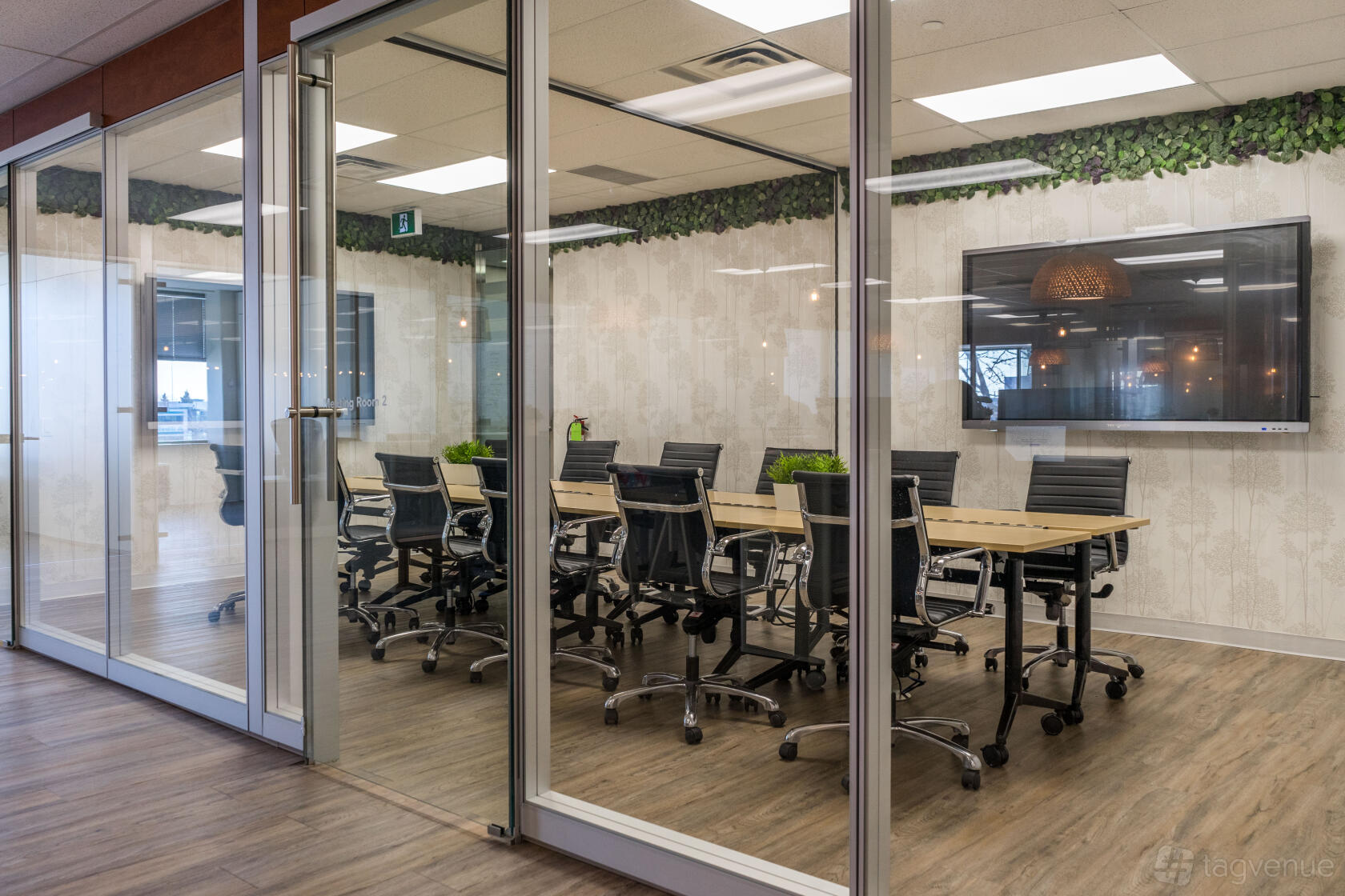 A coworking space meeting room with a long conference table, black chairs, wall-mounted TV, and greenery at Touchdown Coworking.