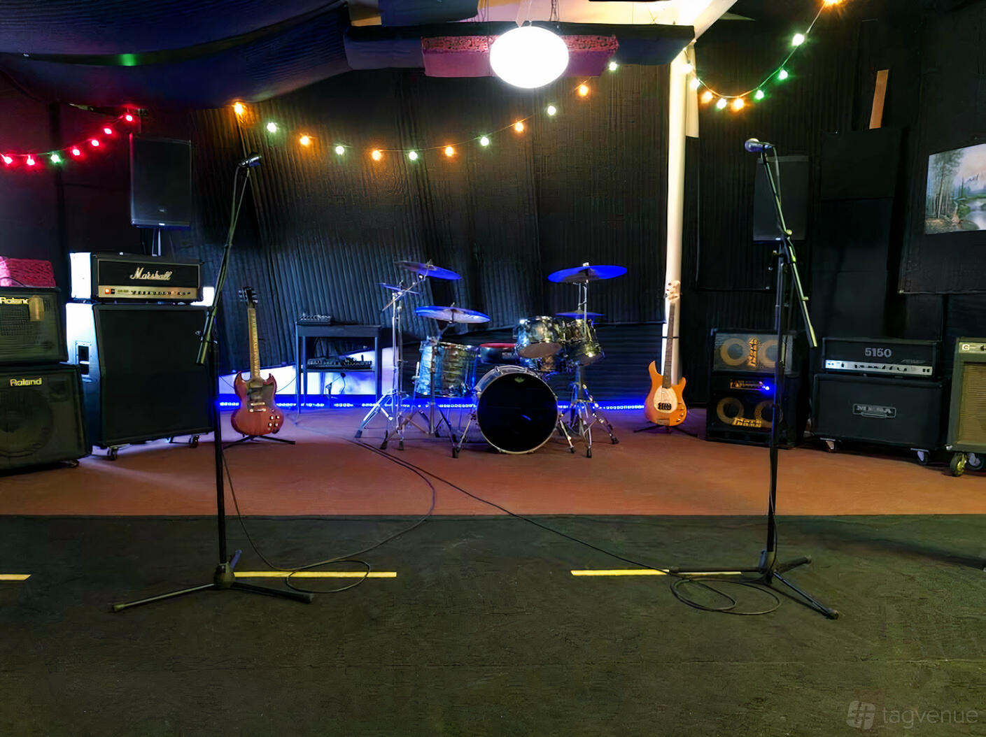 A recording studio with a drum kit, amplifiers, guitars, and colorful string lights at Dark City Studios.