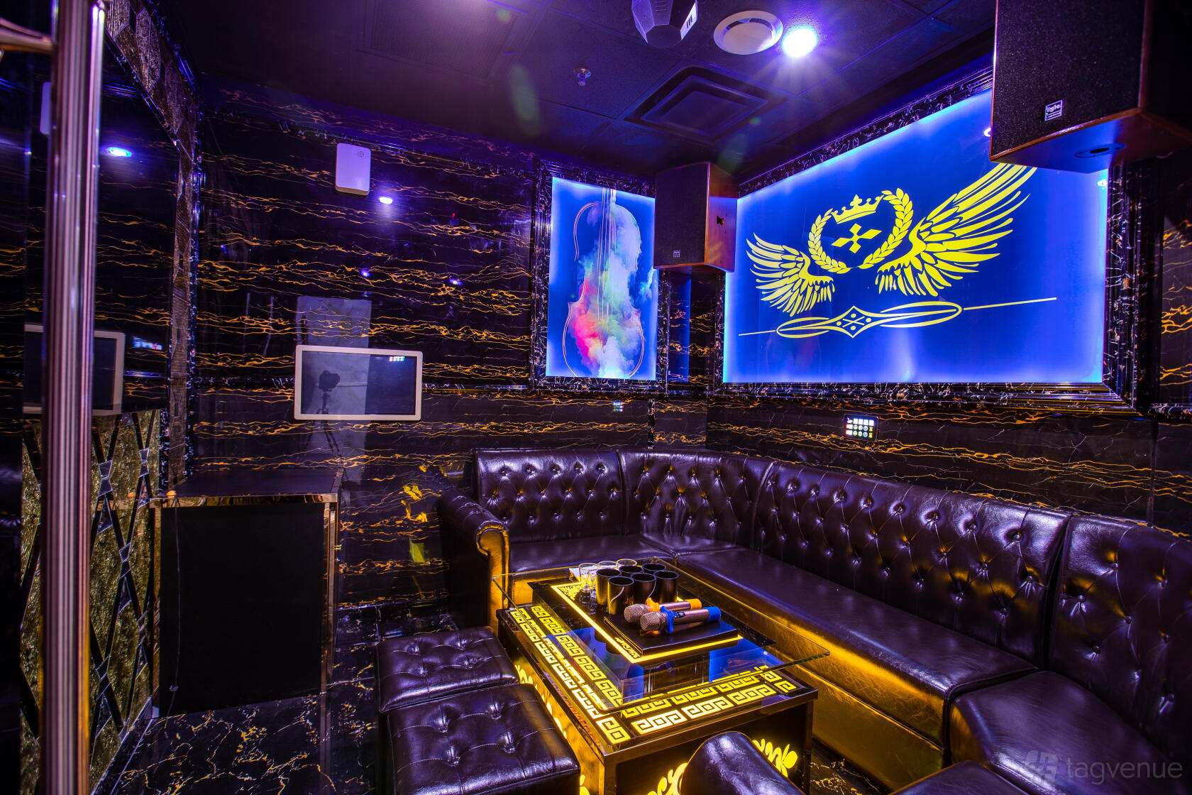 A karaoke bar room with black tufted leather seating, glowing marble table, and neon wall art at Label KTV.