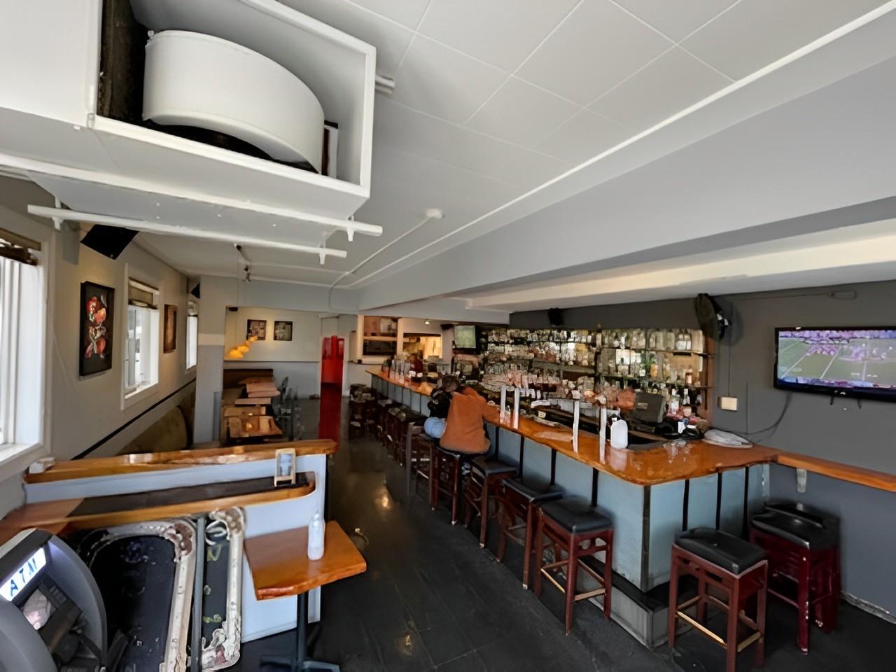 An indoor bar with high stools, a long counter, liquor shelves, and a wall-mounted TV at Mars Bar Restaurant.