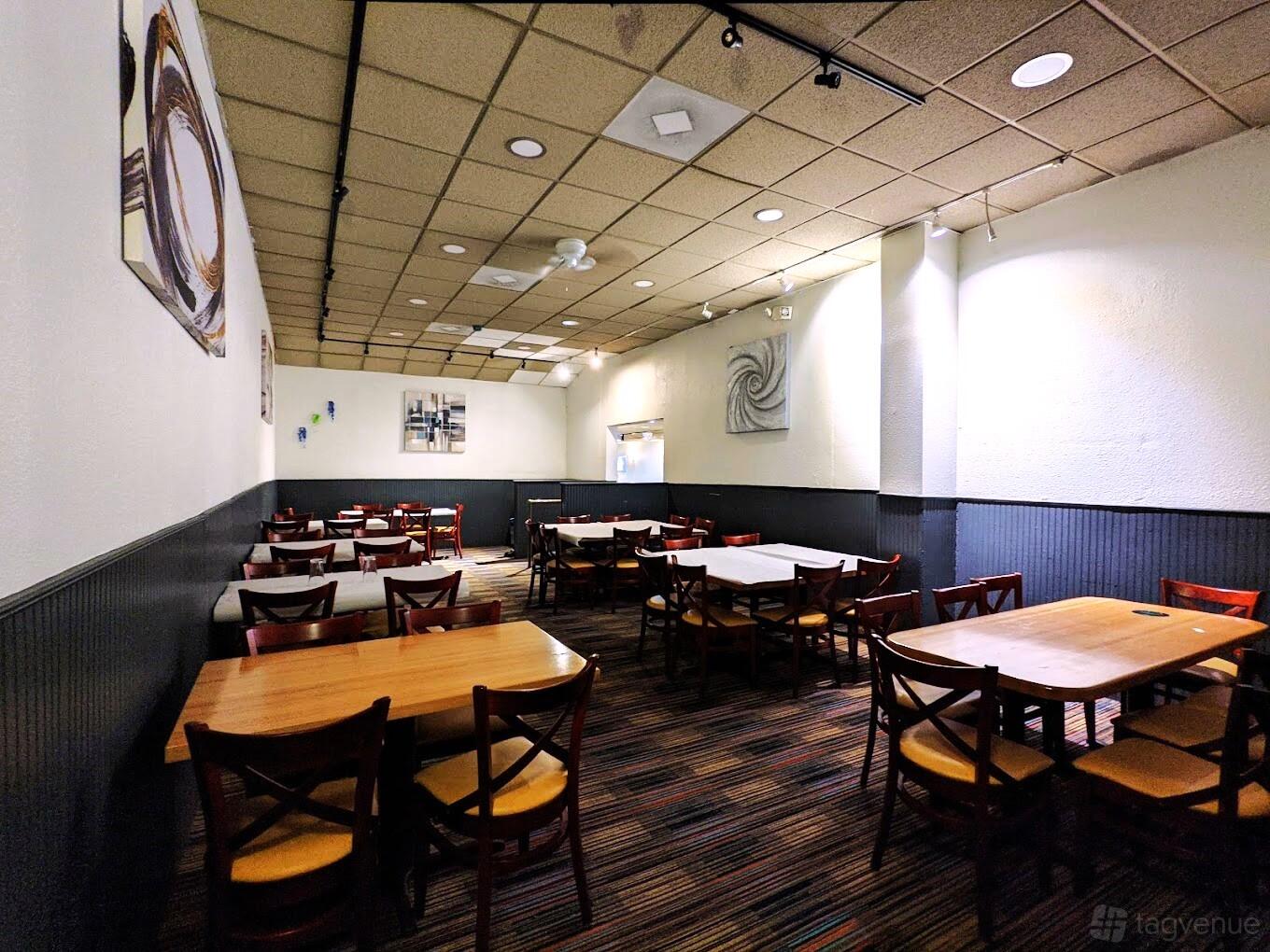 A restaurant with wood tables, cushioned chairs, abstract wall art, and striped carpeting at India Garden.