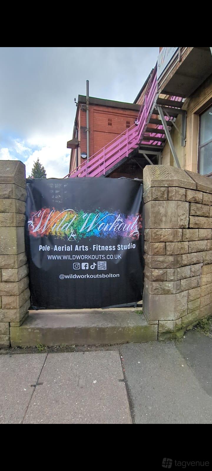 A versatile event space with a banner advertising pole, aerial arts, and fitness next to an outdoor stairway at Wild Workouts.