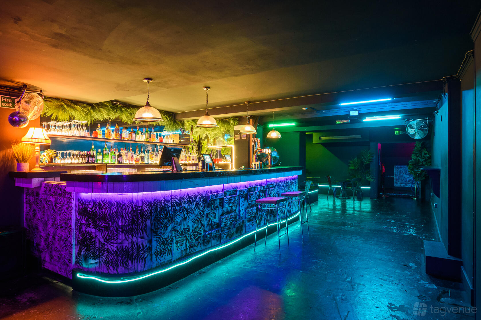 A basement event space with a neon-lit bar, hanging pendant lights, and patterned bar front at Copper Cats.
