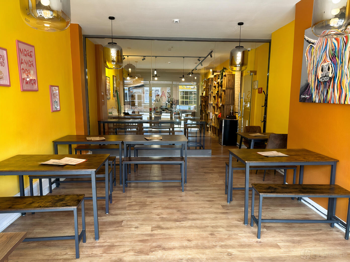 A bar with wood tables, metal chairs, pendant lighting, and bright yellow walls at tapas deli.