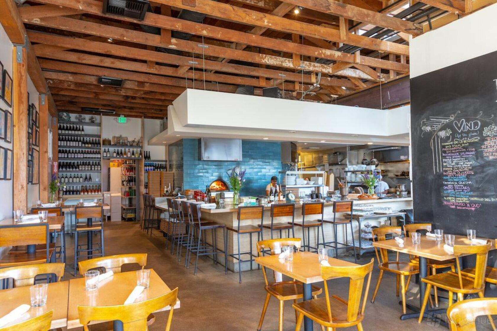 An event space in a restaurant with exposed wooden beams, chalkboard wall, and open kitchen at Milo & Olive.
