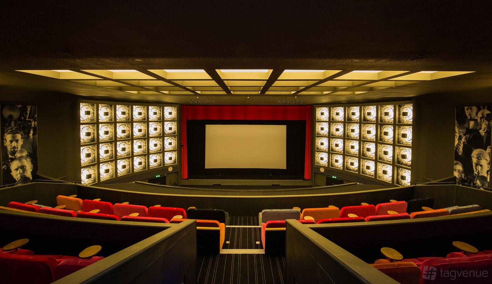 An auditorium with tiered seating, colorful armchairs, illuminated wall panels, and a widescreen at Everyman Esher.