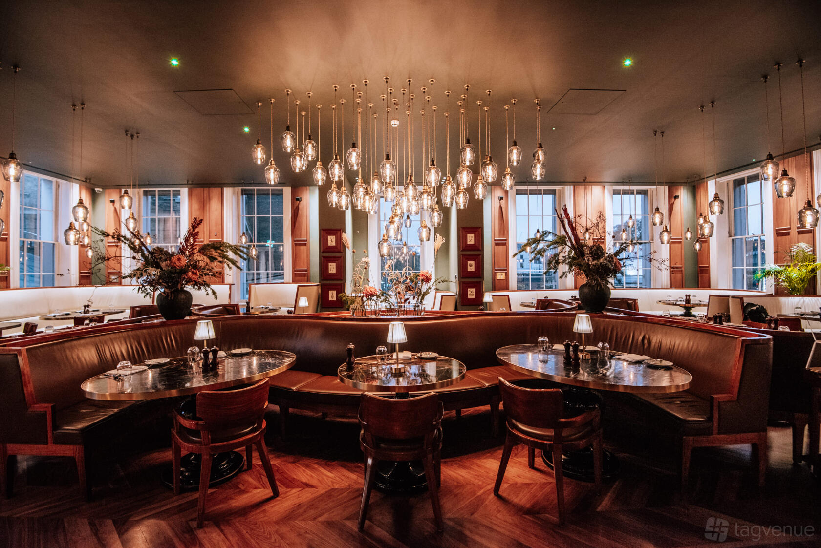 A restaurant with round banquette seating, hanging pendant lights, and large windows at Great Northern Hotel: The Carriage & Lounge.