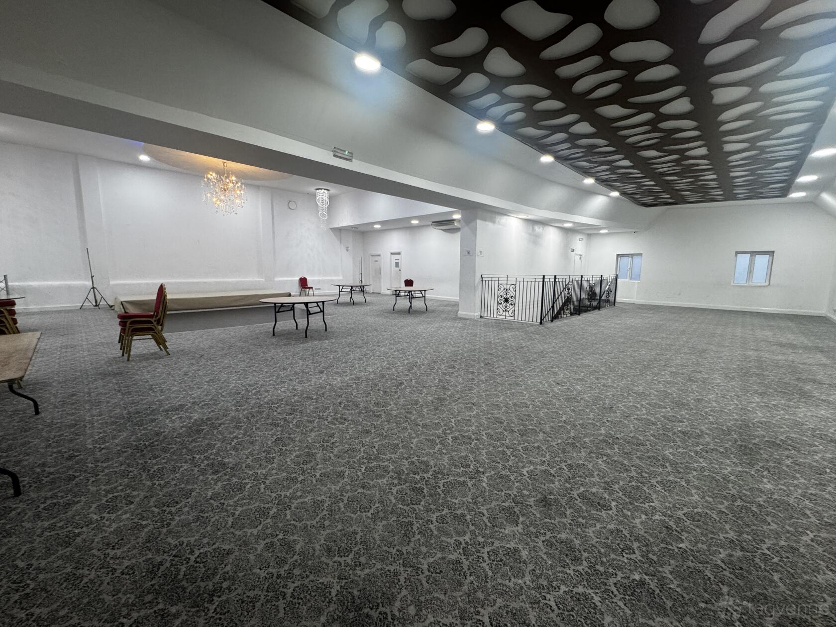 A spacious lounge with patterned carpet, decorative ceiling panels, and a small raised stage at Mayfair Venue.