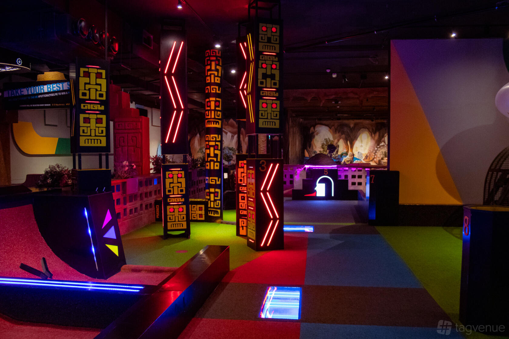 An indoor adventure golf venue with neon-lit columns, colorful turf, and themed decor at Putt Crazy : 18-holes Adventure Golf!