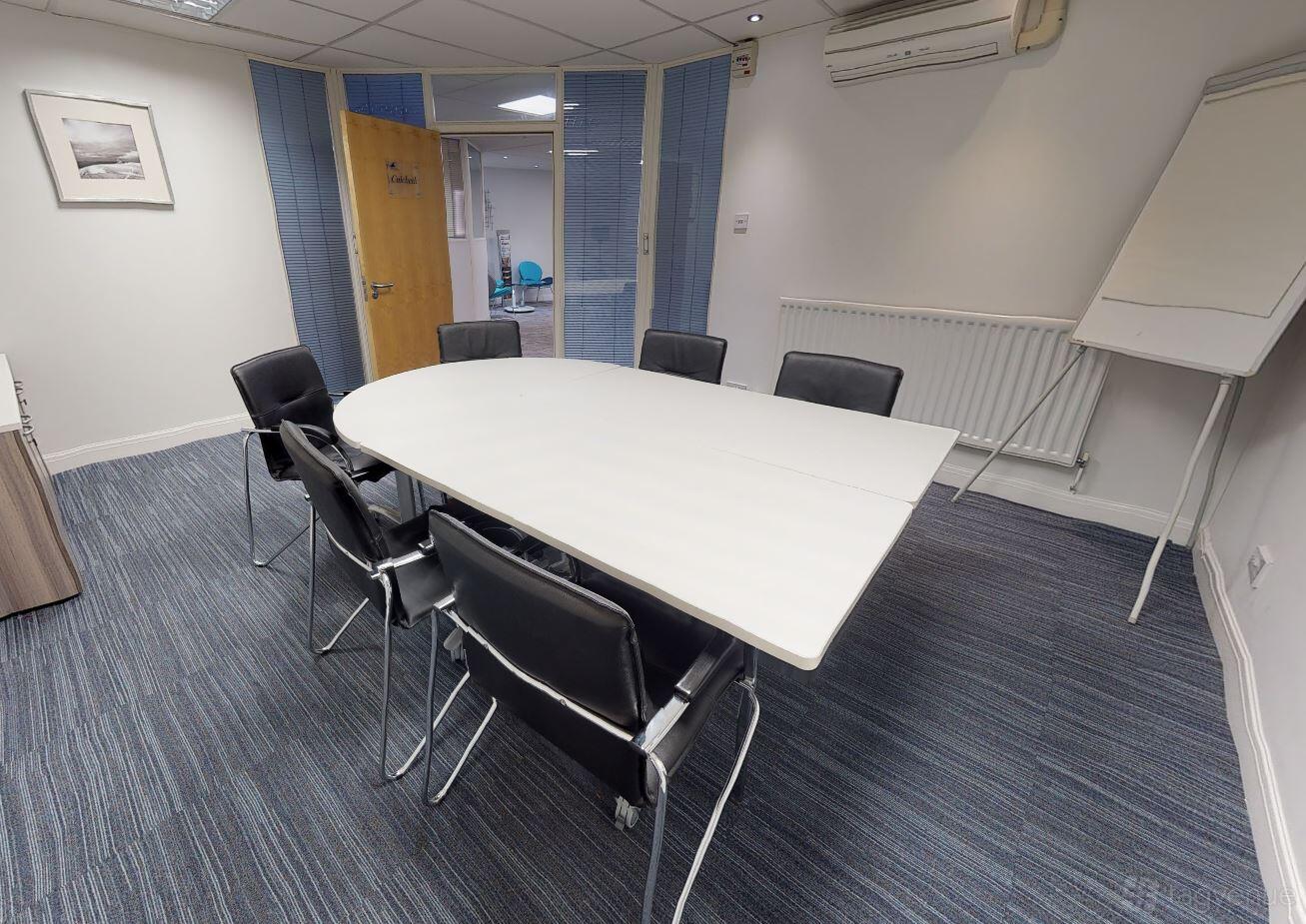 A meeting room with an oval table, six black chairs, glass partitions, and a flipchart at Portal Business Centre Dallam Court.