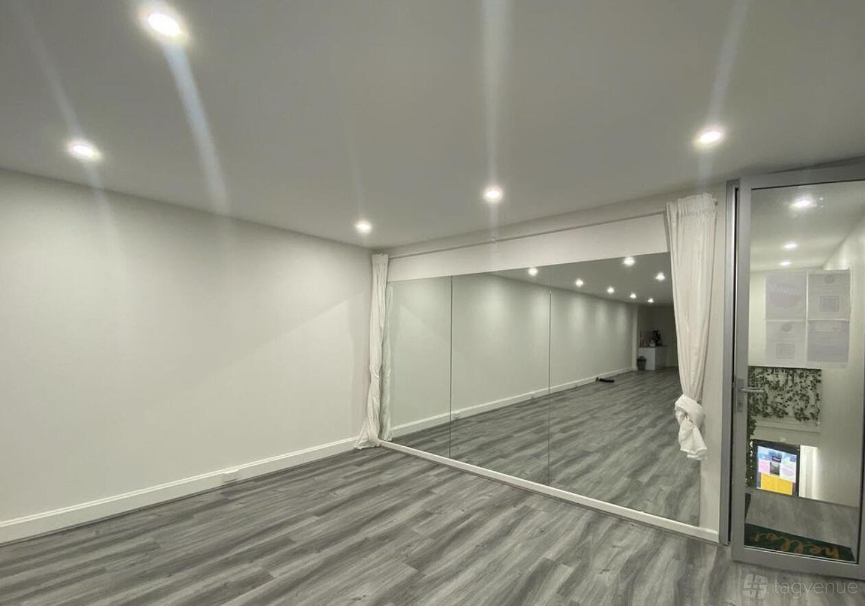 A dance studio with wood-style flooring, wall-length mirrors, recessed lighting, and white curtains at Round dance studio - hurstville.