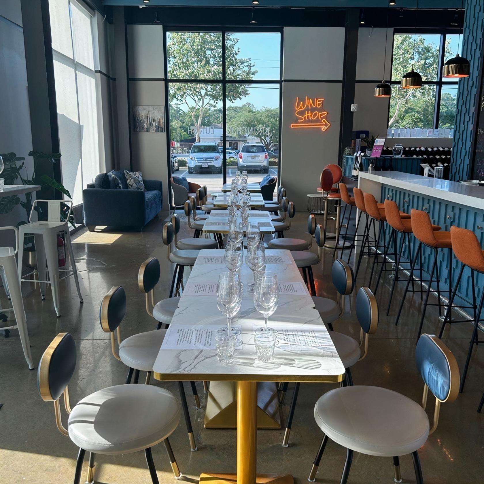 A bar with marble-top tables set with wine glasses and a neon wine shop sign at VinSanto.