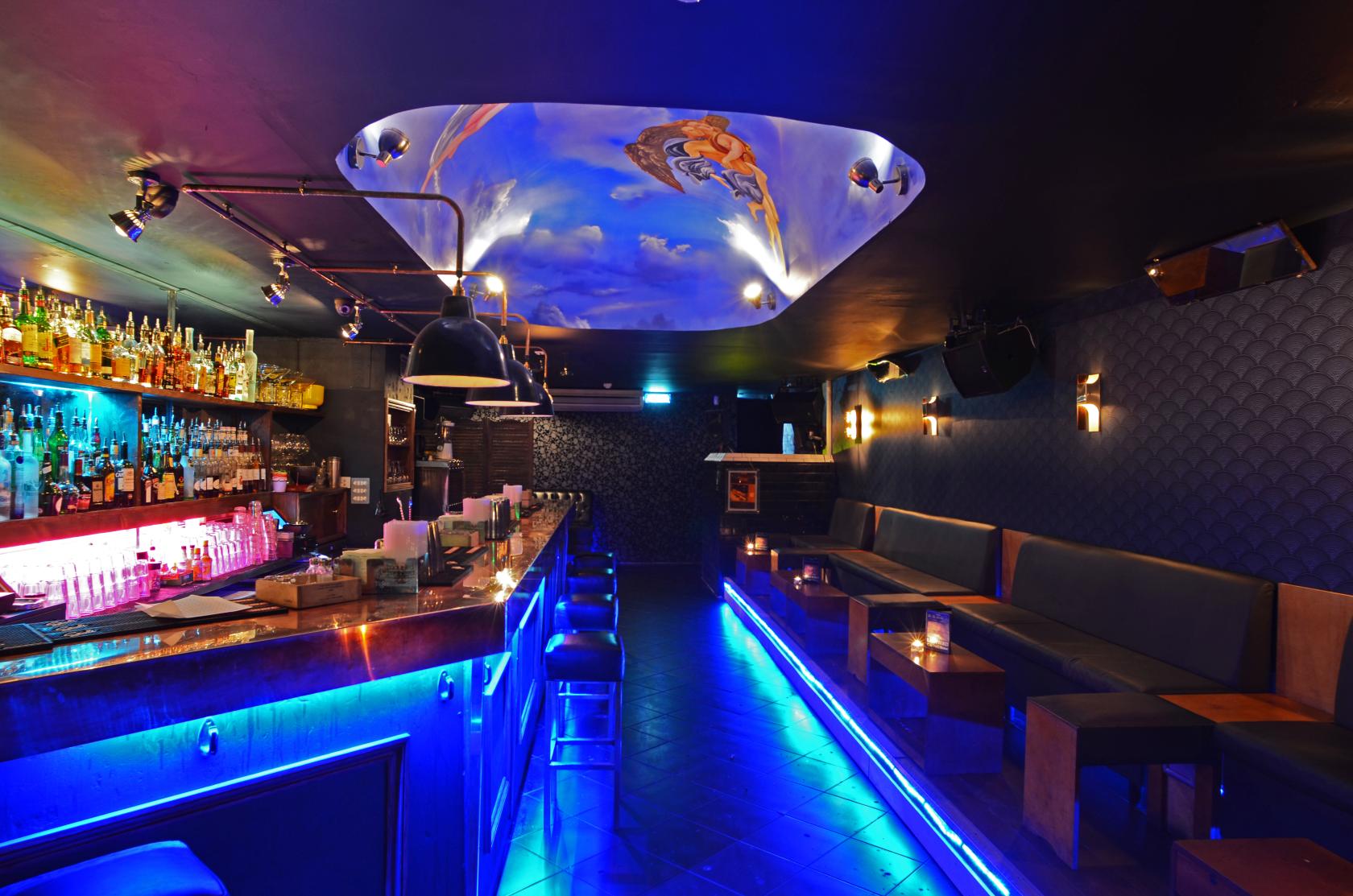 An event space in a cocktail bar with a backlit bar, booth seating, and a painted ceiling at The Ladybird Bar.