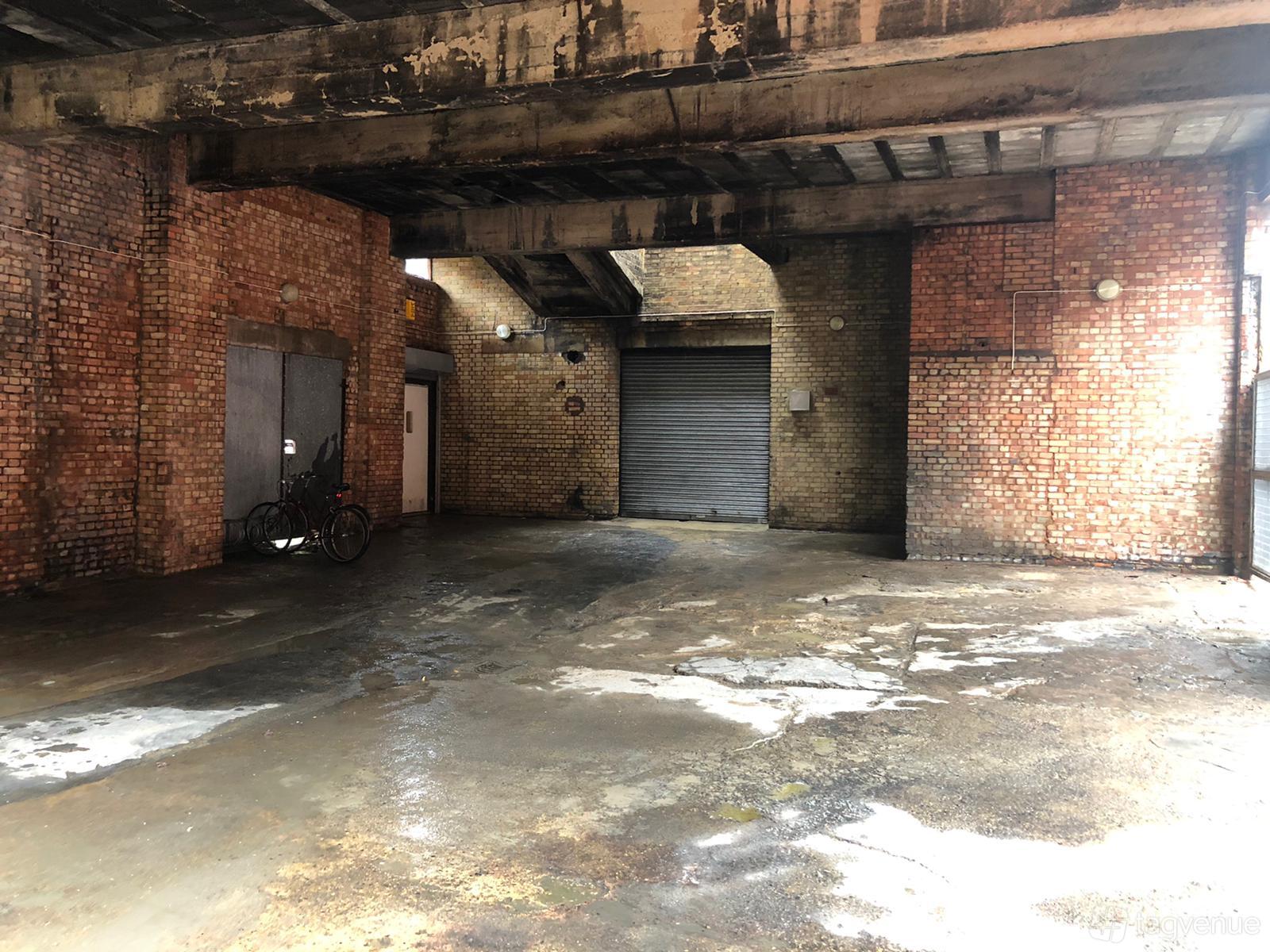 A photo and film studio loading bay with exposed brick walls, concrete flooring, and a large metal roller door at Frederick Terrace.