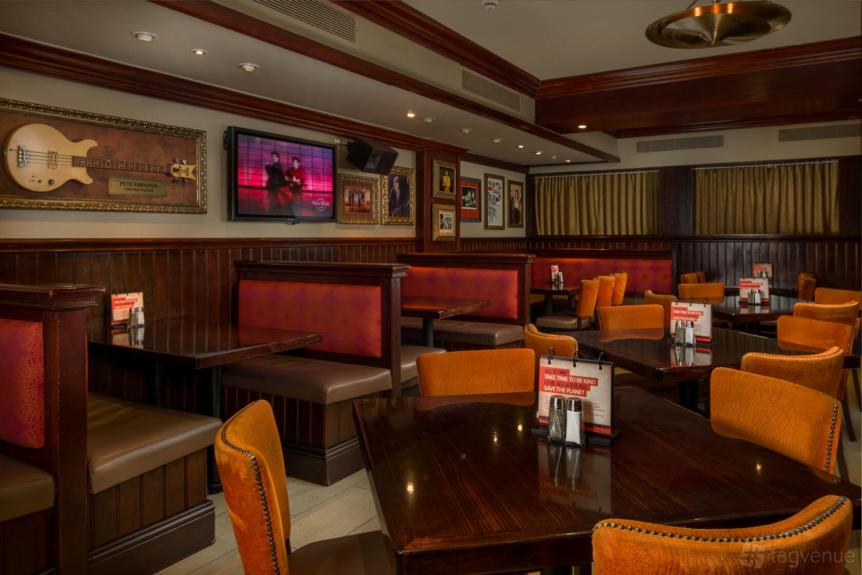 A restaurant with wooden tables, orange upholstered chairs, red booths, and music memorabilia at Hard Rock Cafe Edinburgh.