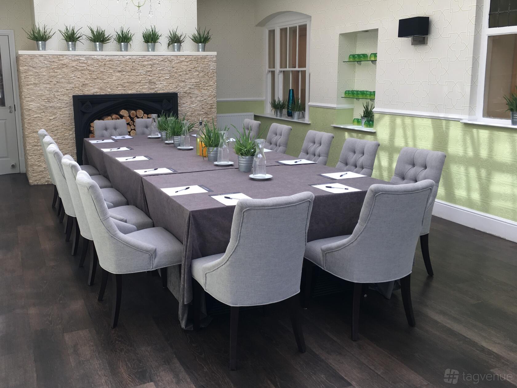 A meeting room with a long table, grey tufted chairs, potted plants, and natural light at The Highworth Hotel.