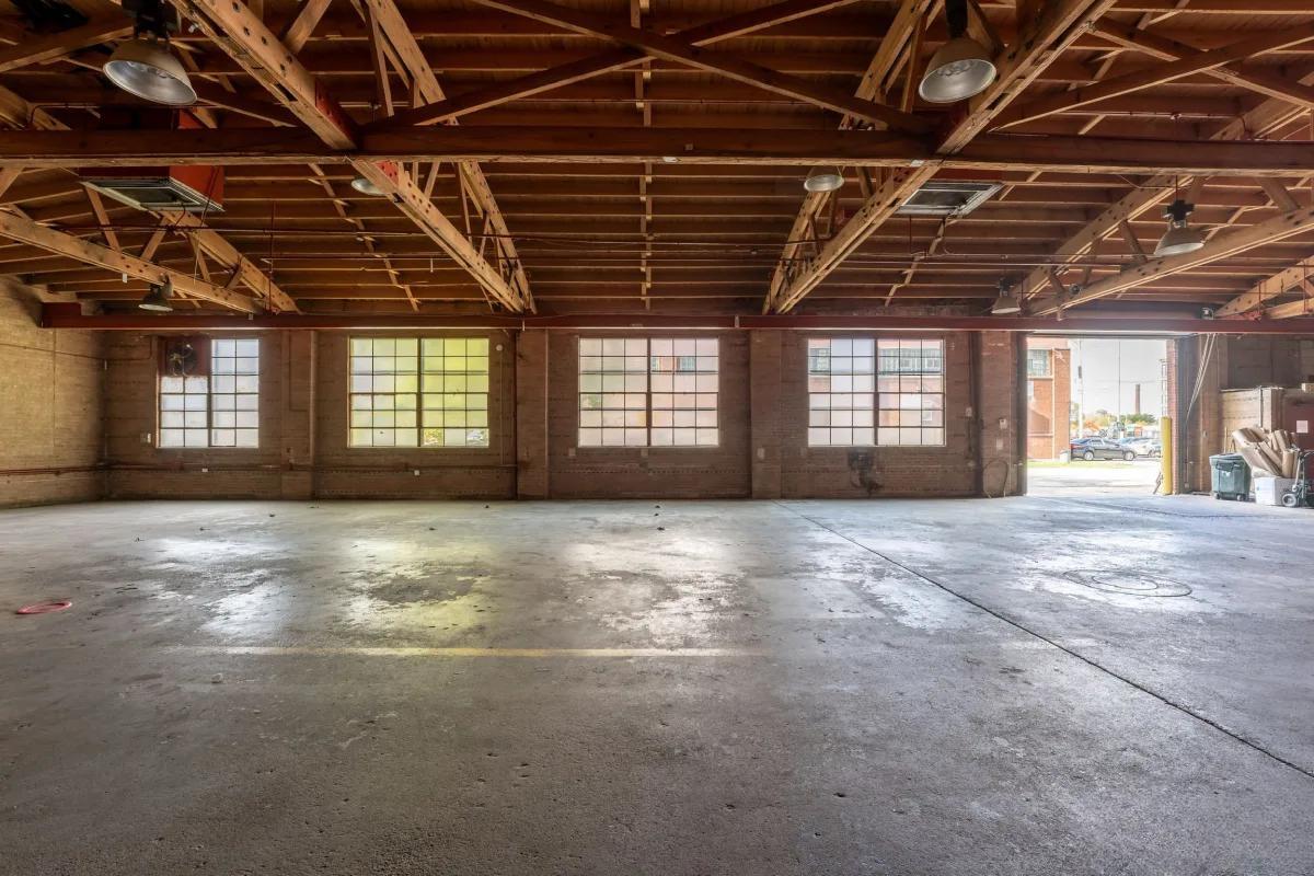 A spacious warehouse with exposed wood beams, concrete floor, and large grid windows at Parker Karlov Events.