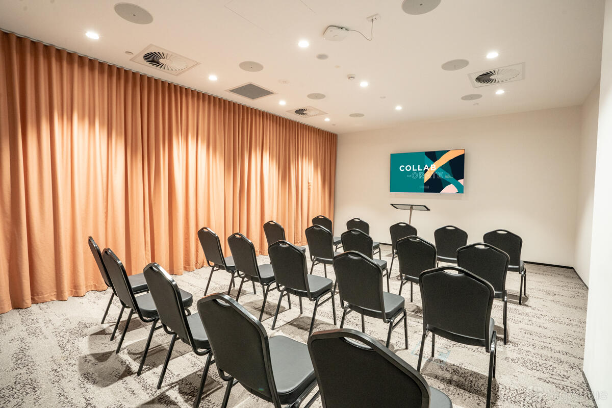 A training room with theater-style black chairs, a digital presentation screen, and floor-to-ceiling curtains at Waterman at Eastland.