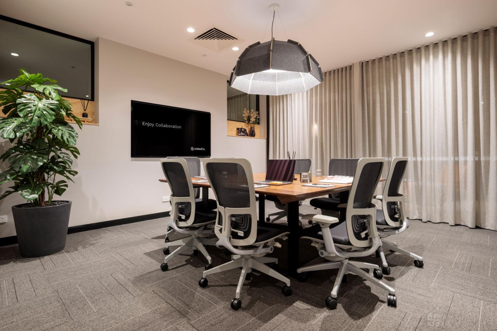 A meeting room with a long wooden table, ergonomic chairs, and a large pendant light at United Co. Fitzroy.