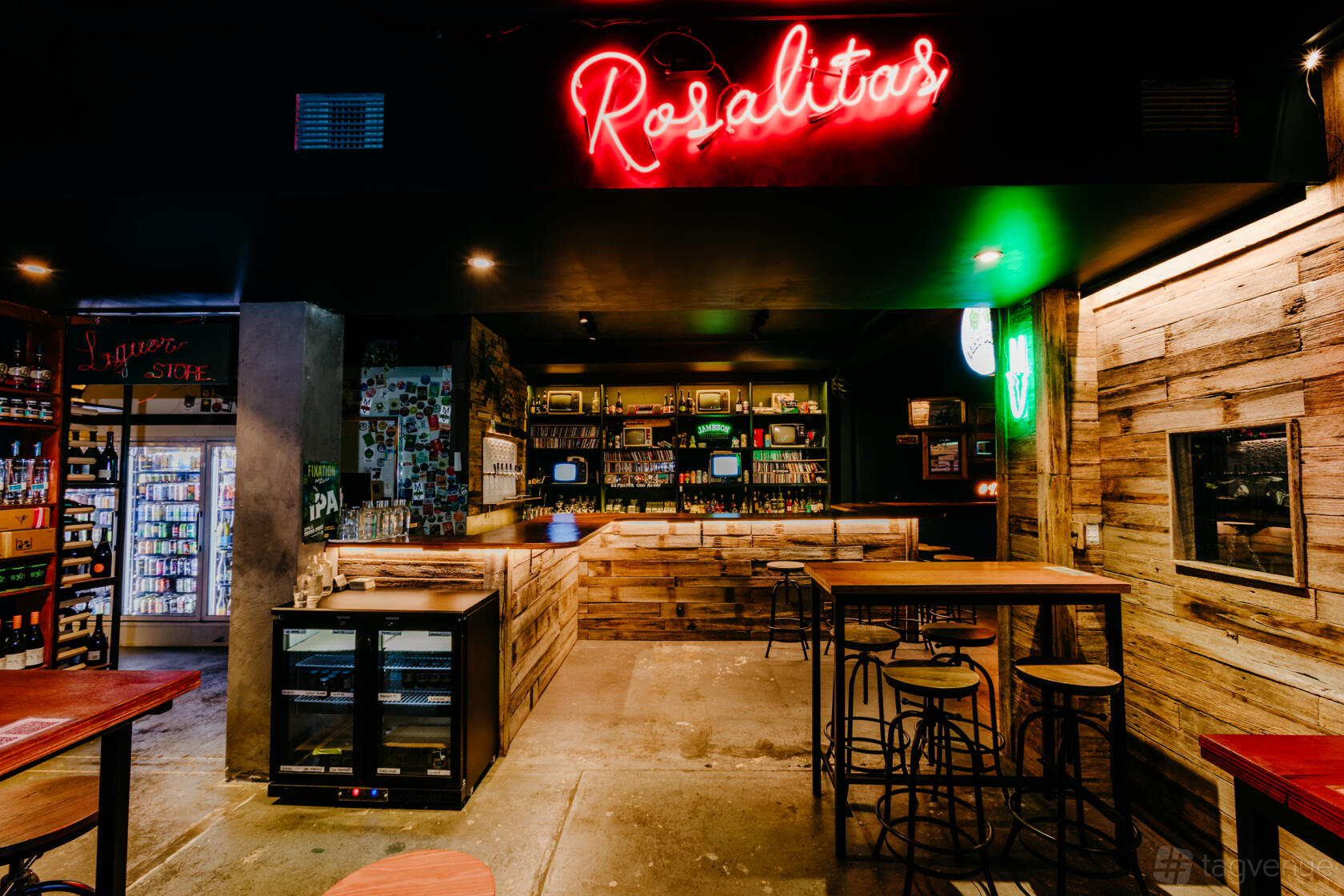 An event space in a pub with a rustic wooden bar, neon Rosalitas sign, and high tables at East Of Everything.