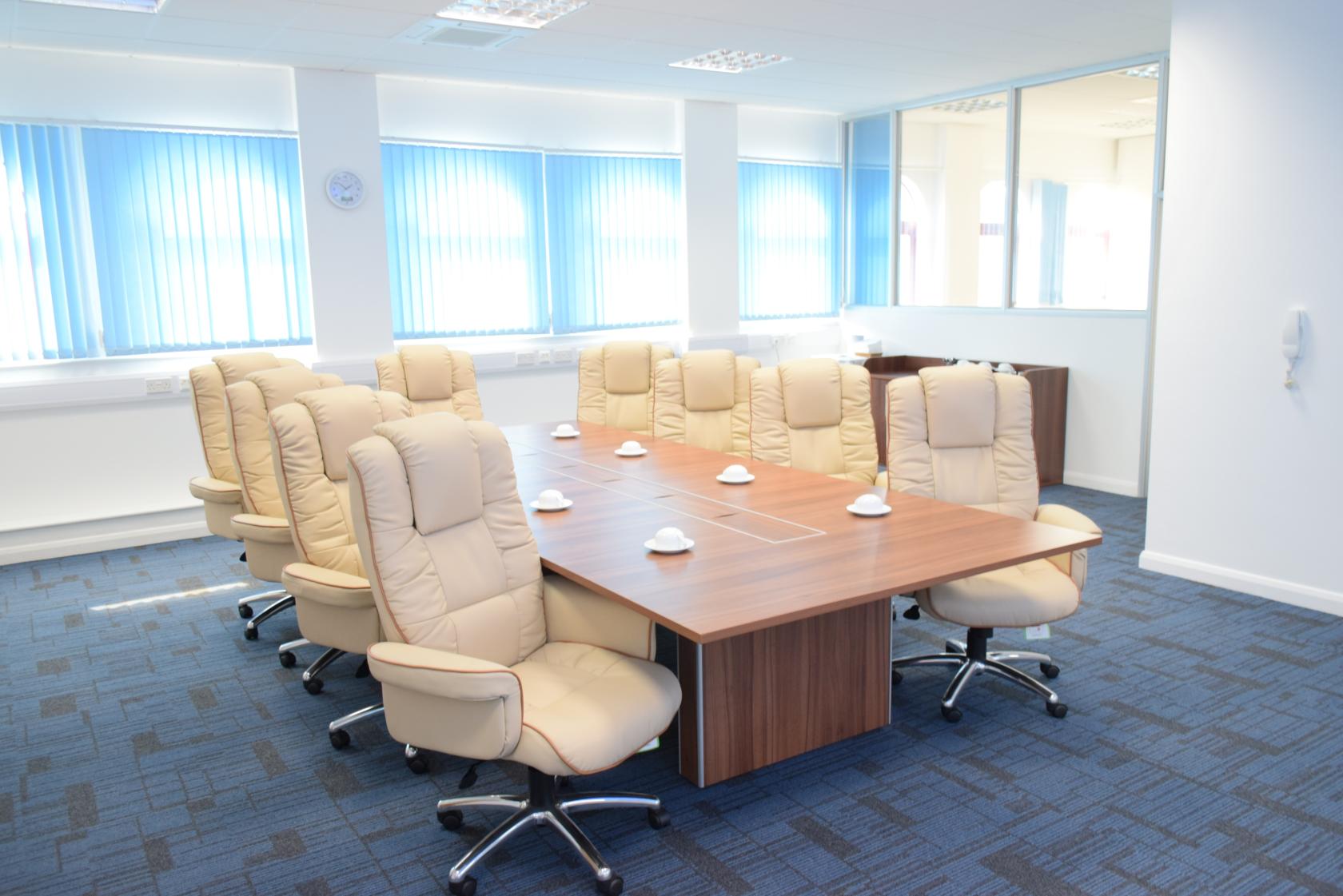 A boardroom with a long wooden table, high-back cream chairs, and blue carpet at Humanitarian Academy for Development.