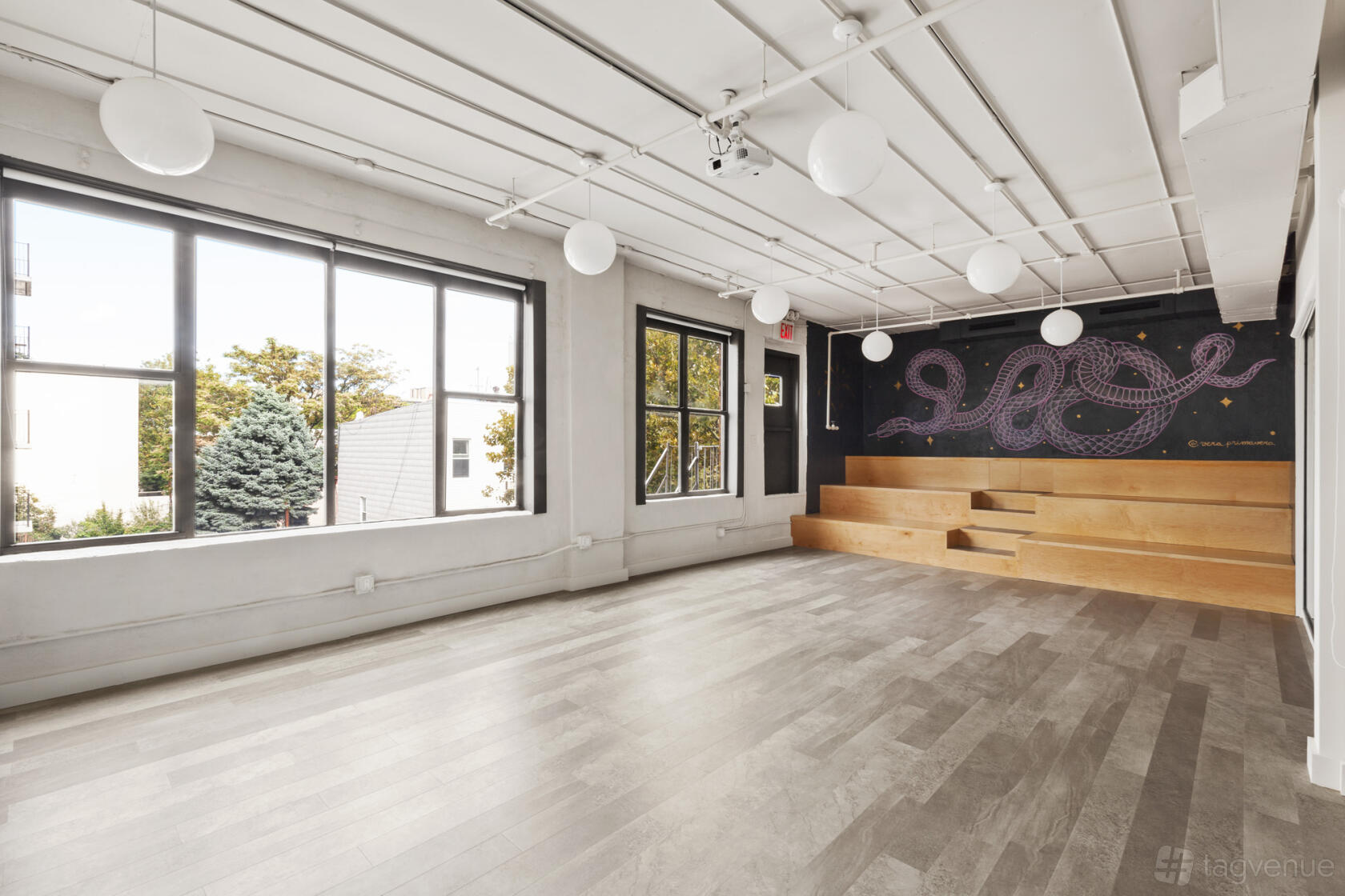 An event space with large windows, light wood flooring, and tiered seating with a mural at CLASS & CO.