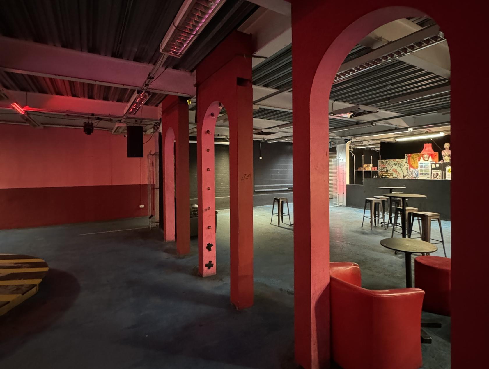 A warehouse nightclub with exposed ceilings, red pillars, and scattered high tables at Low Profile Studios.