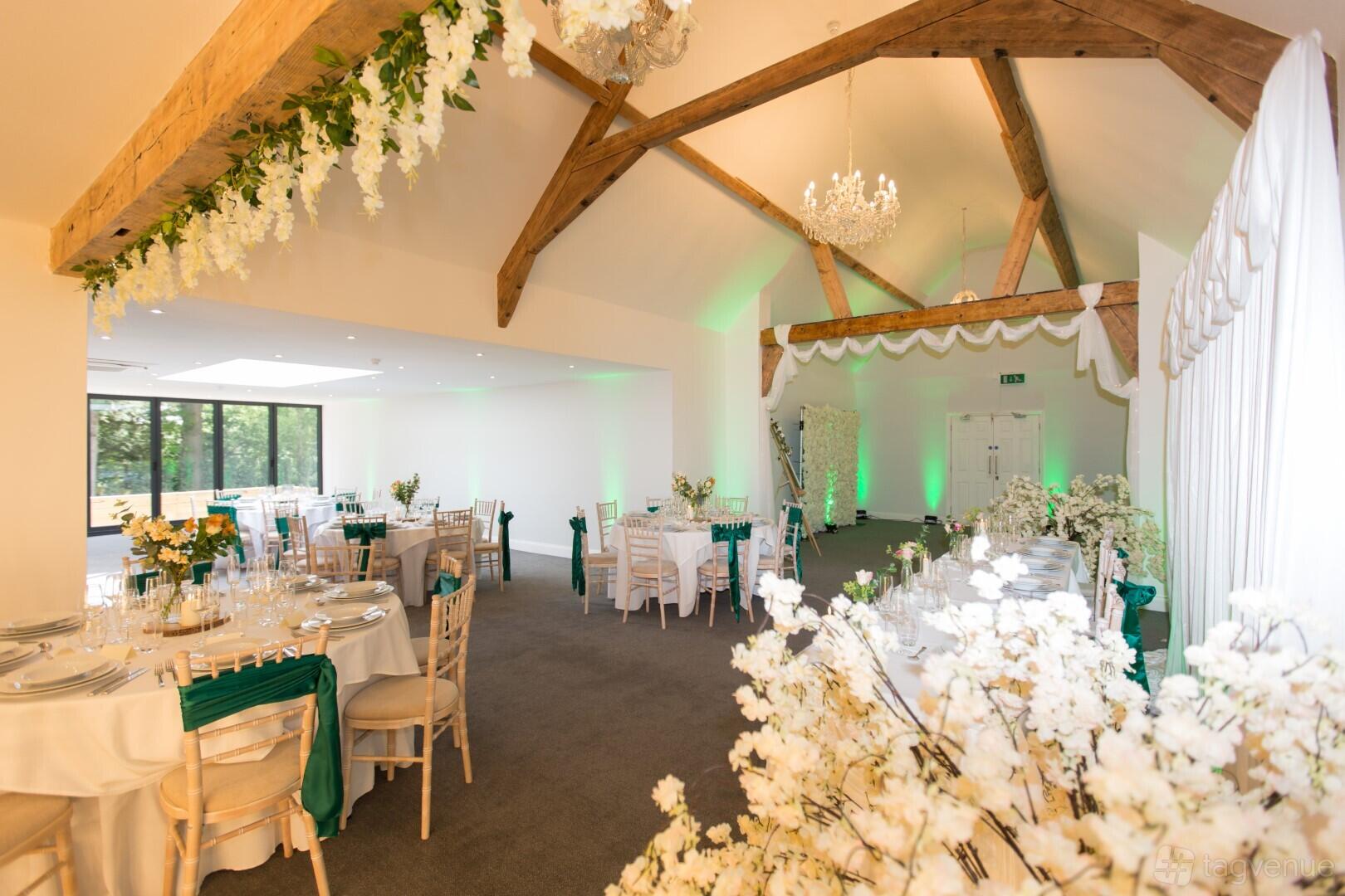 A hotel event suite with exposed wooden beams, round tables with white linens, and floral arrangements at The Angel Hotel.