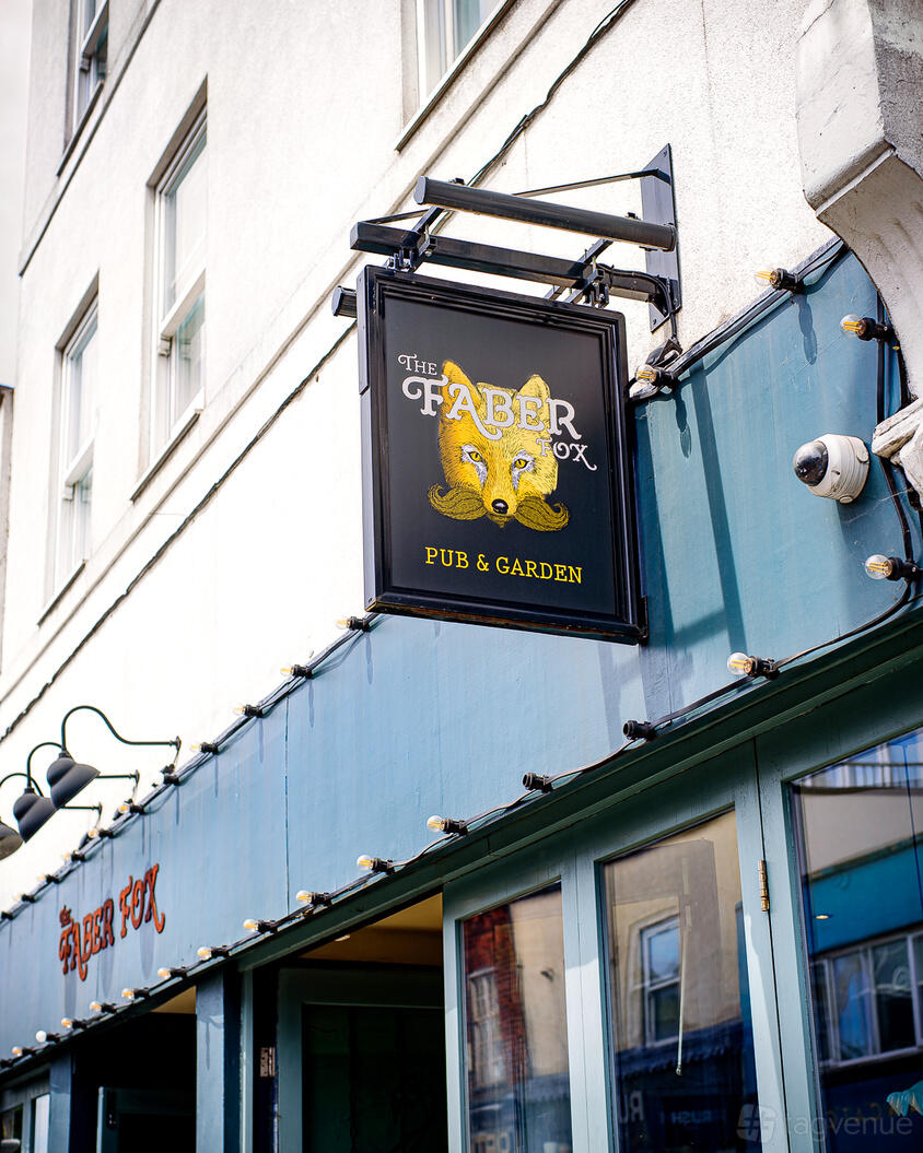 An outdoor pub sign with a fox illustration mounted above a blue awning at The Faber Fox.
