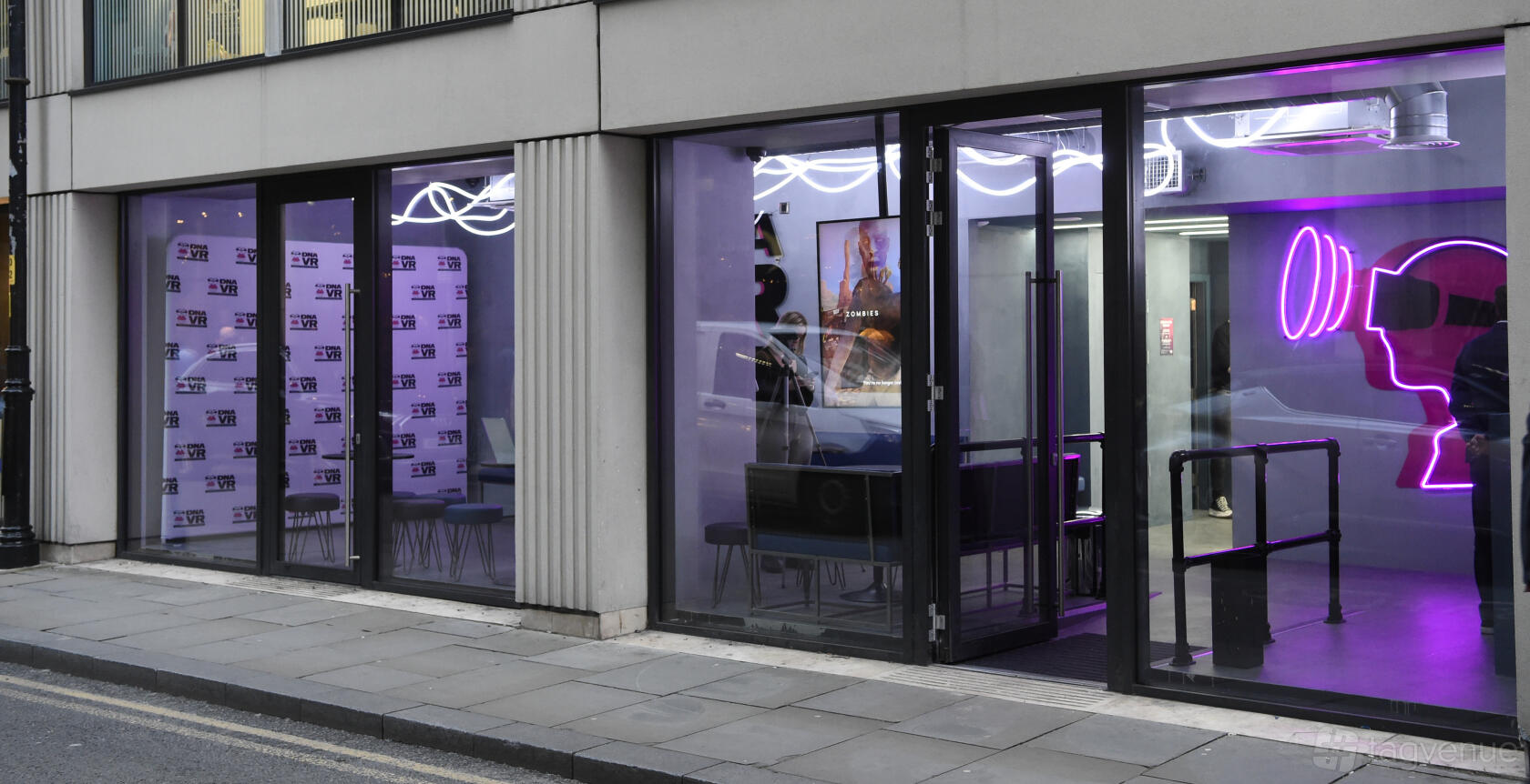 A versatile event space with floor-to-ceiling windows, neon lighting, and promotional banners at DNA VR Manchester.