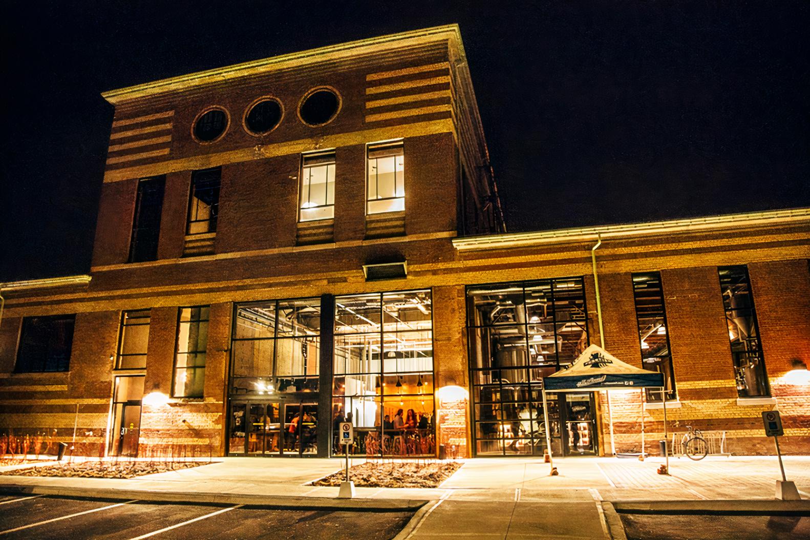 A brick pub with large windows and warm exterior lighting at night at Junction Craft Beverage Co.