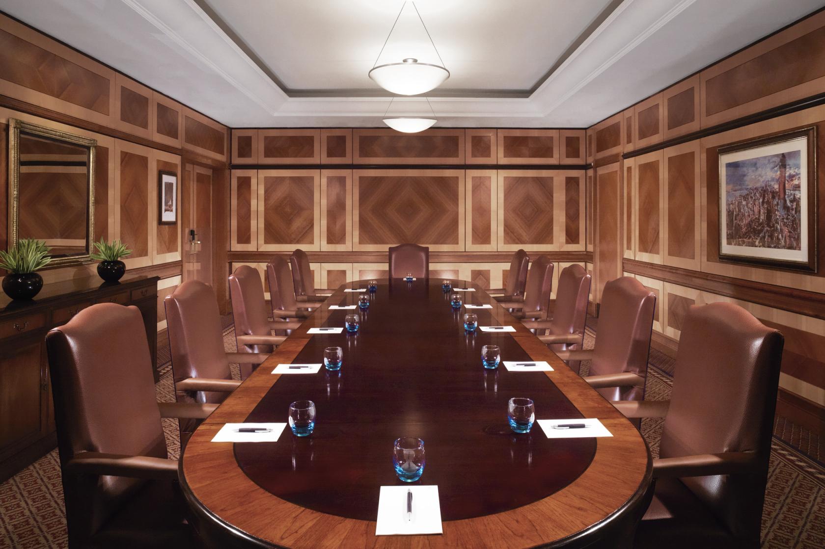 A meeting room with a polished oval table, leather chairs, wood panel walls, and ceiling lights at Sheraton Skyline Hotel London Heathrow.