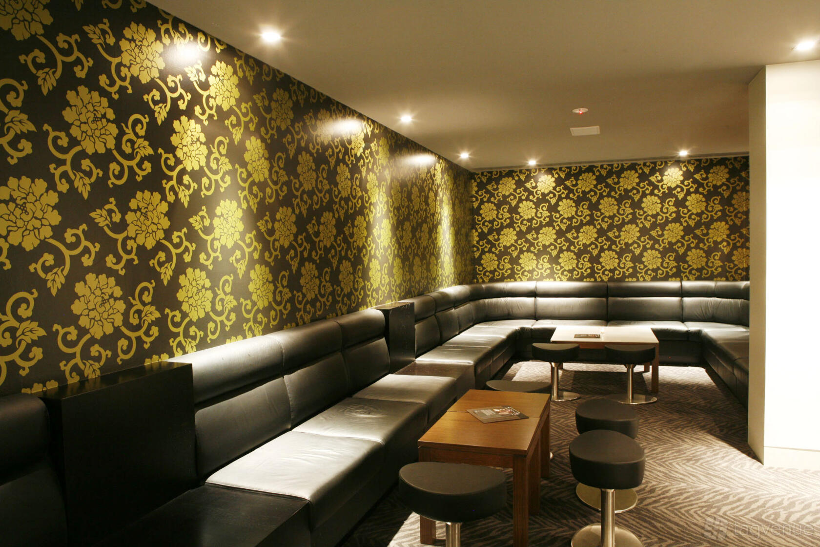 An event space in a pub with black leather banquette seating, patterned wallpaper, and low tables at The Precinct Hotel.